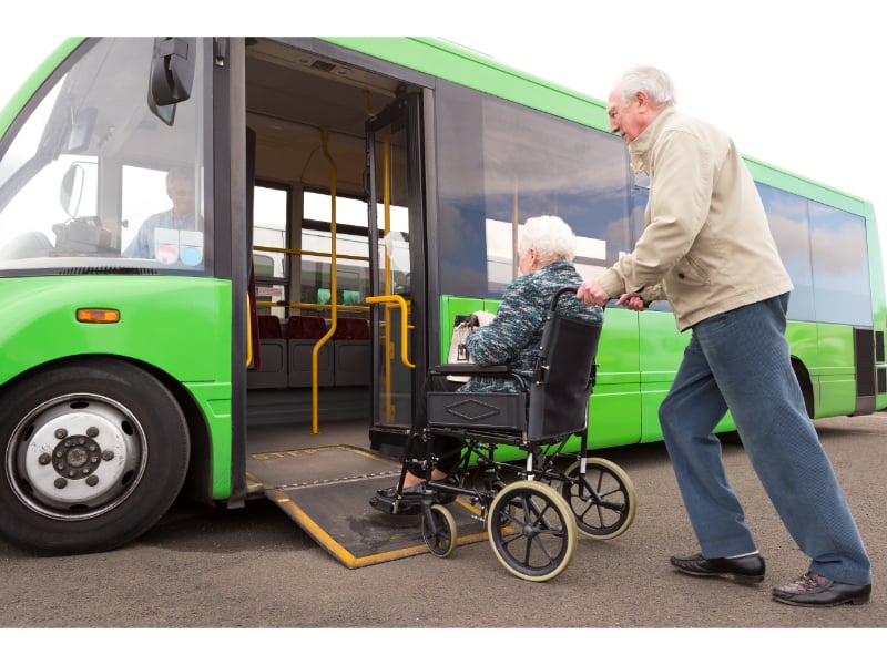 Older adult pushes another older adult in a wheelchair onto a city bus wheelchair ramp