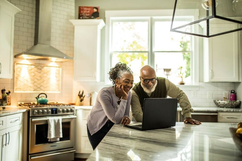 Older adult couple in the kitchen on a laptop