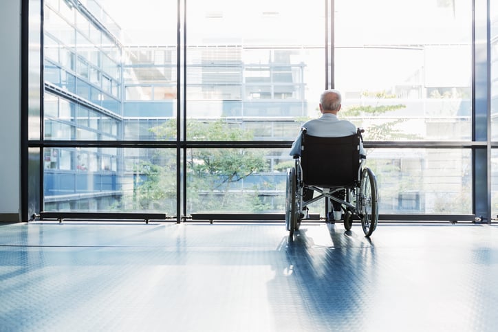 Older adult in a wheelchair is left alone in a hallway.